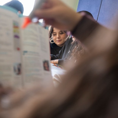 Ein Mädchen hält ein Schulheft hoch und markiert mit einem orangefarbenen Edding eine Stelle. Es ist eine Szene aus der kostenlosen Hausaufgabenbetreuung beim Verein Kölner Appell gegen Rassismus.