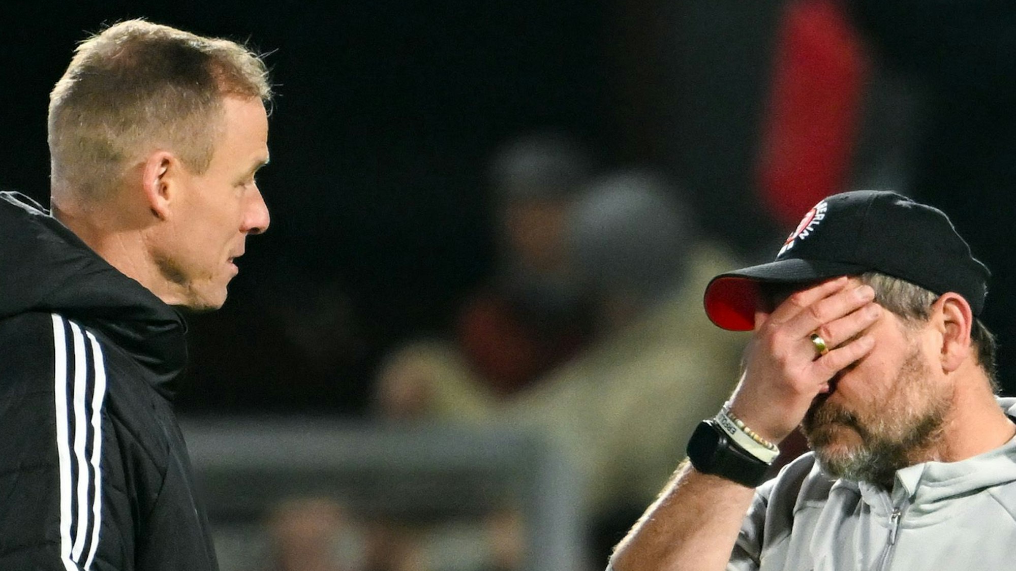 Zwei Männer, von denen der rechte eine Hand vor sein Gesicht hält, besprechen sich.