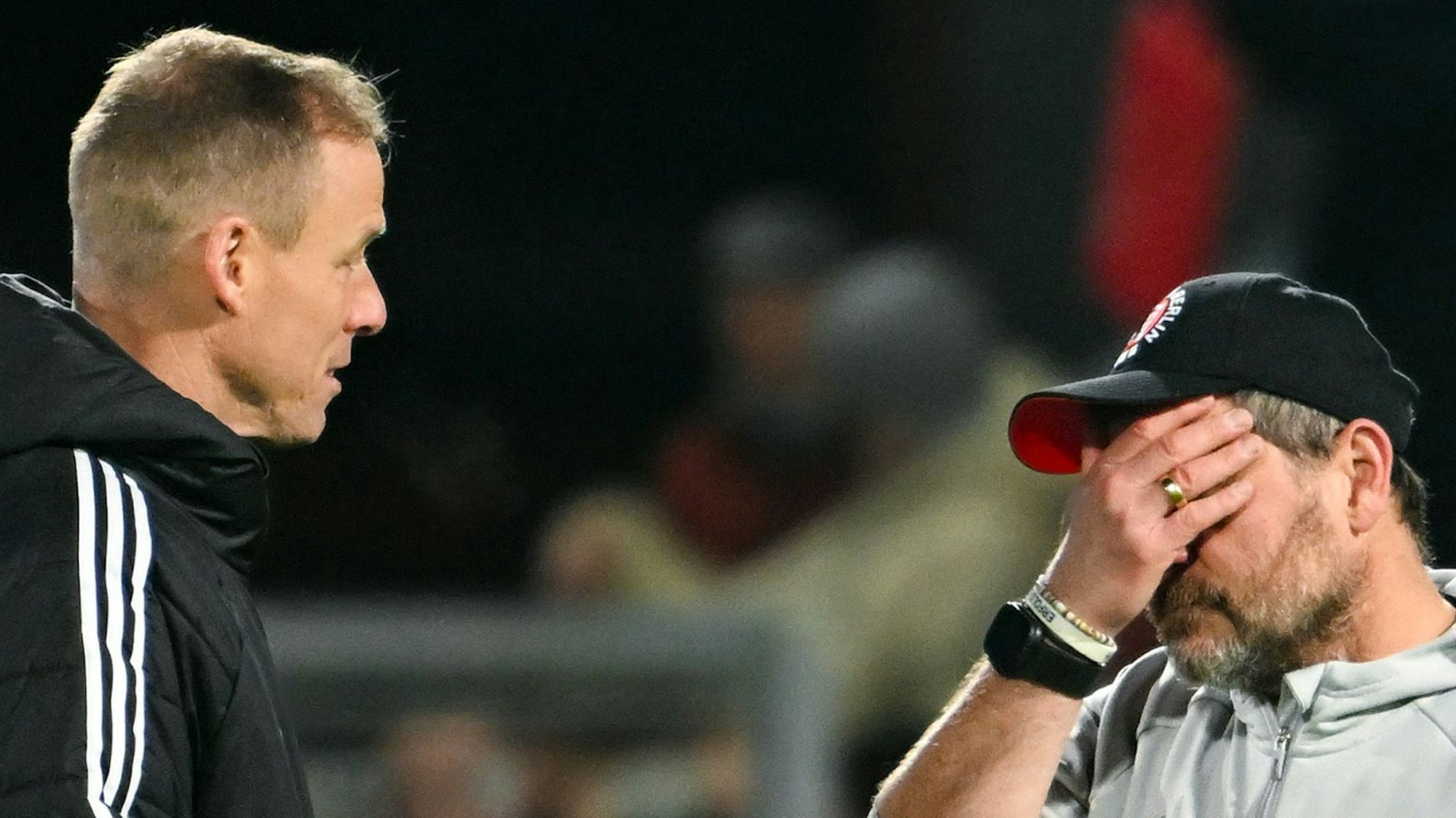 Zwei Männer, von denen der rechte eine Hand vor sein Gesicht hält, besprechen sich.