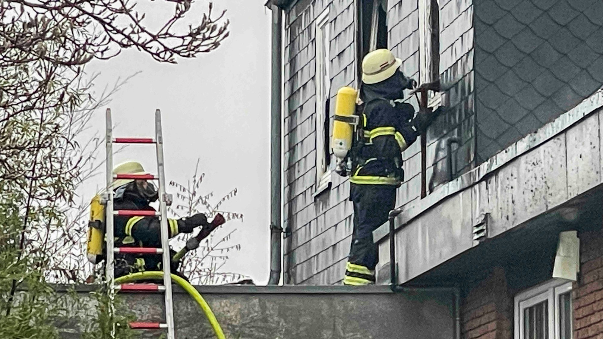 Das Bild zeigt einen Feuerwehrmann, der mit einem Werkzeug die Fassade des Hauses öffnet.
