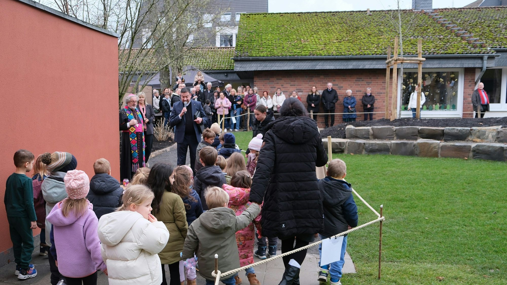 Auf einem Weg entlang einer mit einer Kordel abgesperrten Rasenfläche stehen viele Erwachsene und Kinder.
