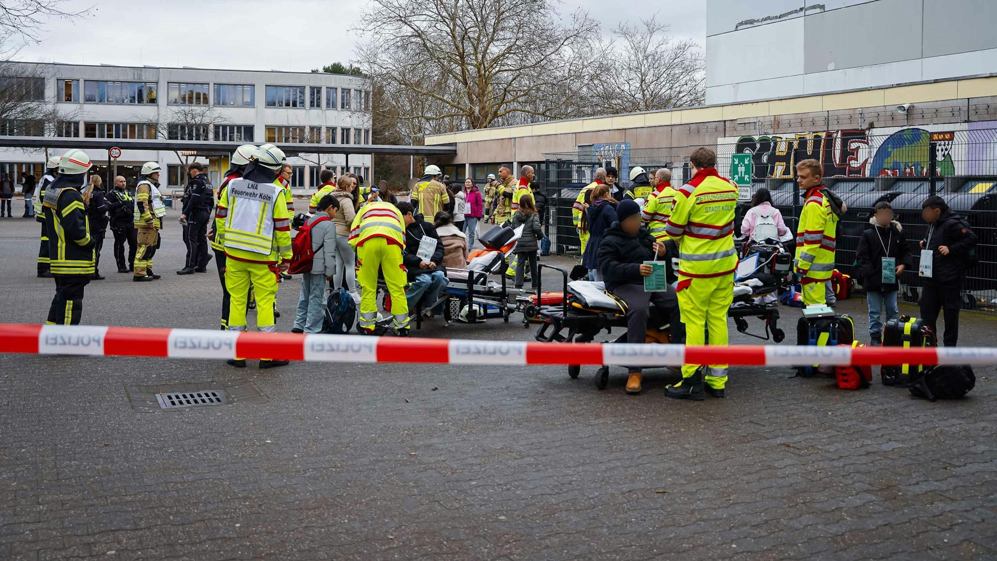 Kräfte von Feuerwehr und Rettungsdienst kümmern sich auf einem Schulhof um Schülerinnen und Schüler.