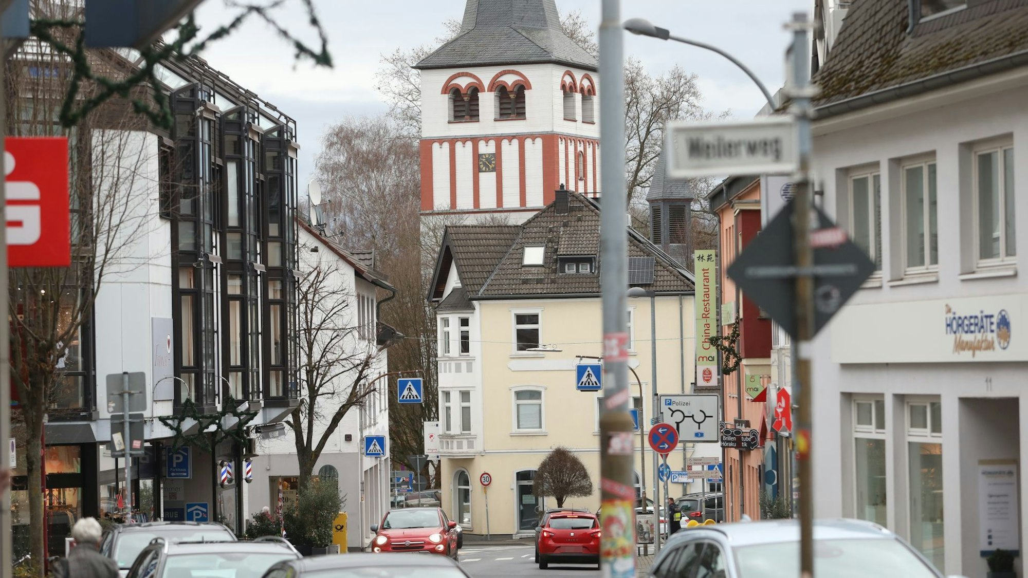 Autos auf einer Geschäftsstraße, im Hintergrund eine Kirche.