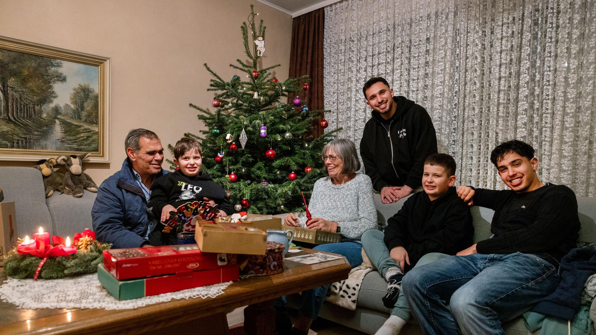 Vater Ebraheem Raslan, Daniel Raslan, Heidrun Brandt, Nedal Raslan, Talal Raslan und Mohammed Raslan sietzen gemeinsam auf dem Sofa. Dahinter steht der geschmückte Weihnachtsbaum, auf dem Tisch liegen die Kartons.