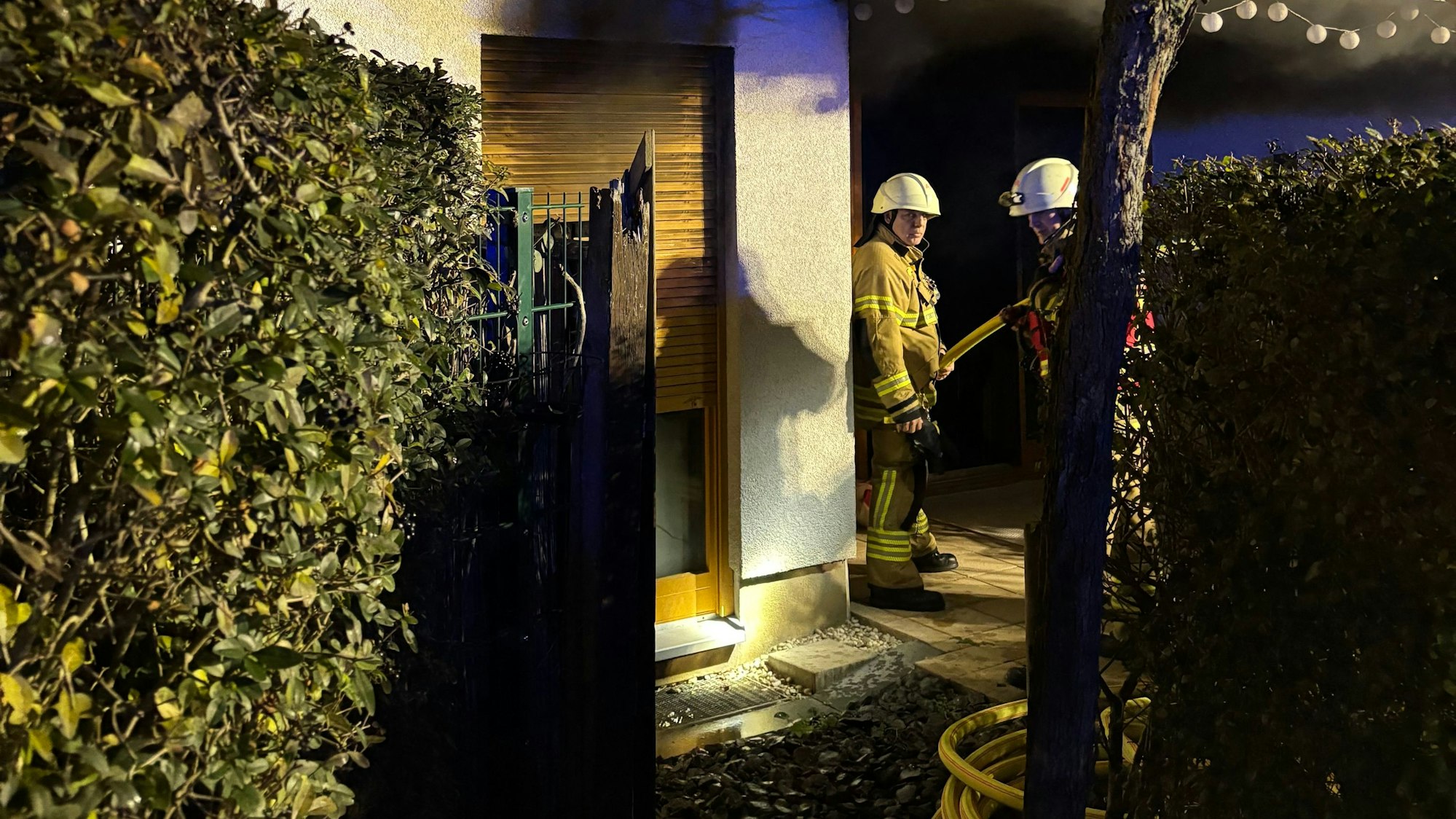 Das Bild zeigt zwei Feuerwehrmänner vor einem Mehrfamilienhaus