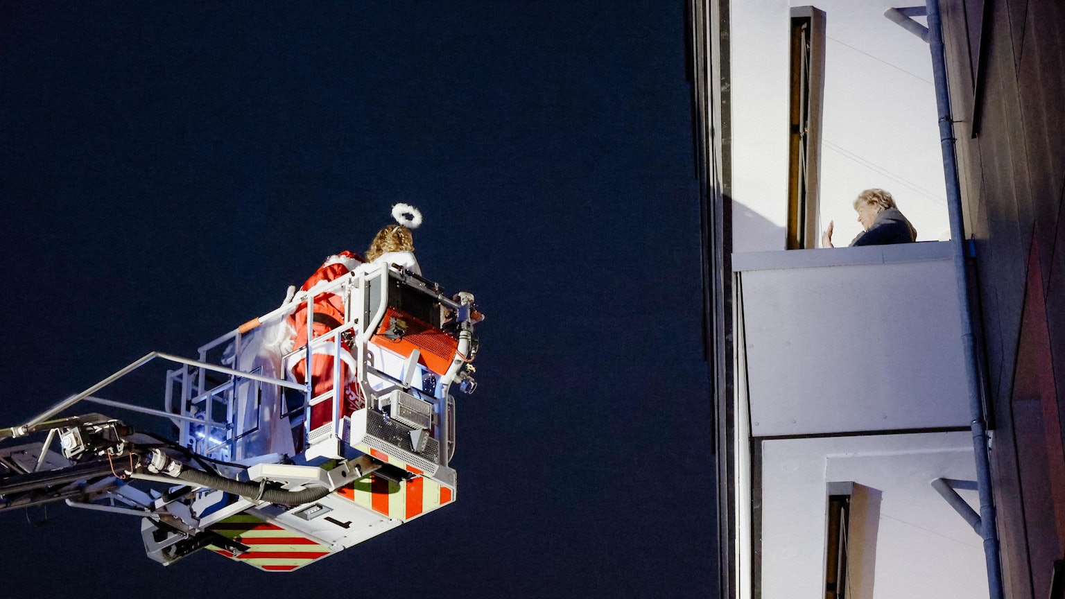 Der Weihnachtsmann grüßt eine Frau, er ist mit einer Drehleiter unterwegs.