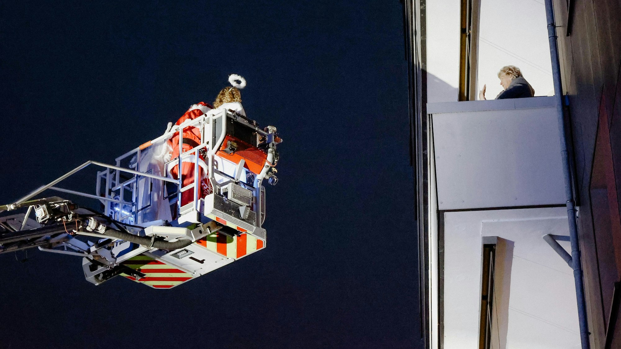 Der Weihnachtsmann grüßt eine Frau, er ist mit einer Drehleiter unterwegs.