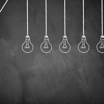 Sechs gemalte Glühbirnen, eine leuchtet.