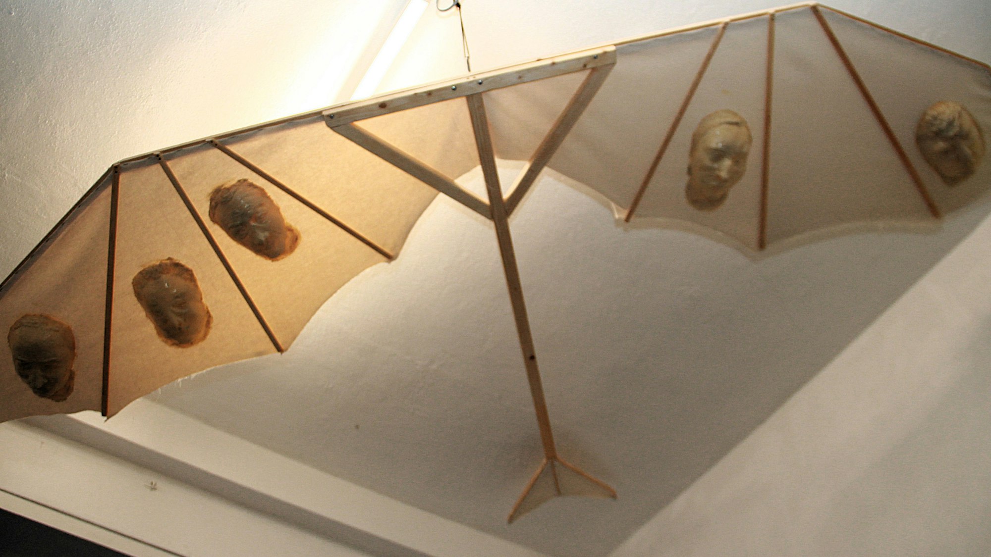 Eine Art Drachen mit einem Holzgestell ist an der Decke eines Altbau-Raumes befestigt.