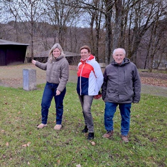 Zwei Frauen und ein Mann stehen auf einer Wiese am Freilinger See. Im Hintergrund ist eine Grillhütte.