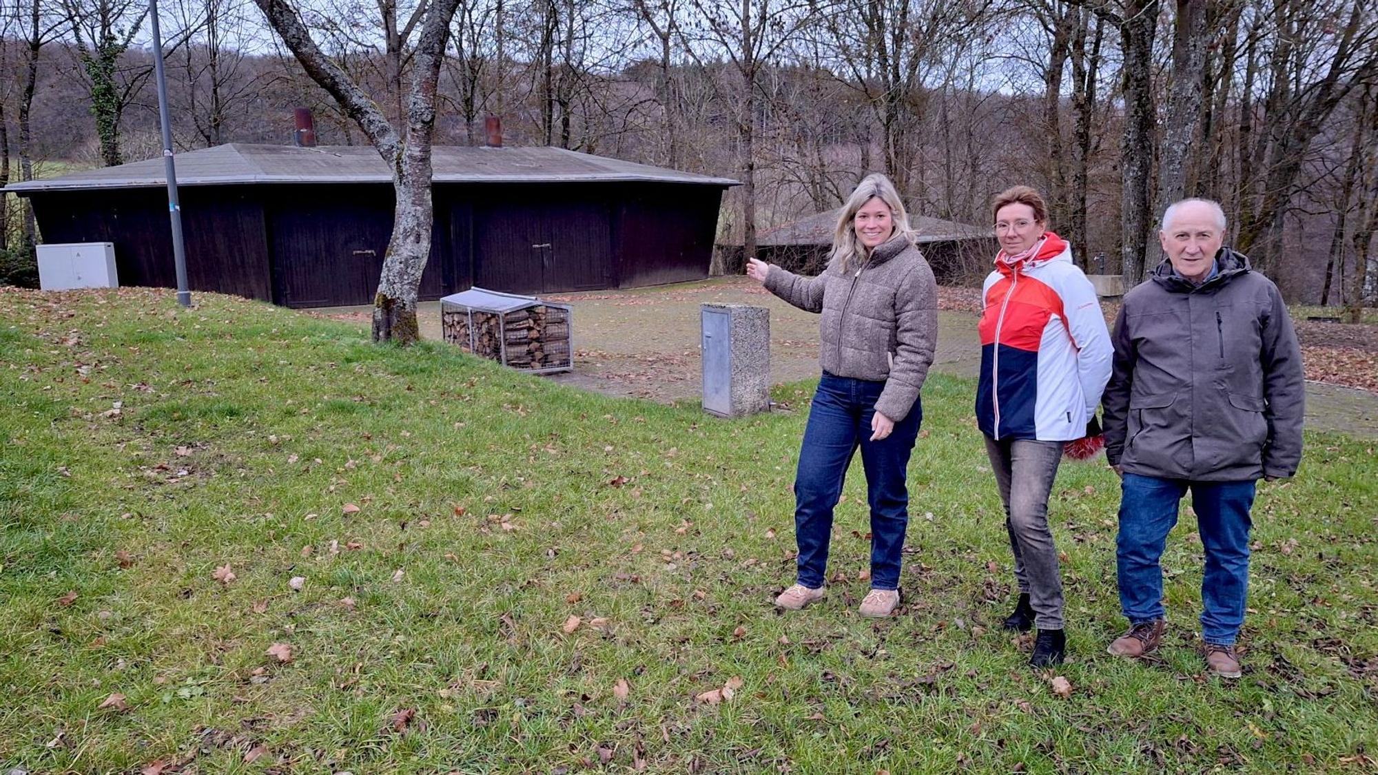 Zwei Frauen und ein Mann stehen auf einer Wiese am Freilinger See. Im Hintergrund ist eine Grillhütte.