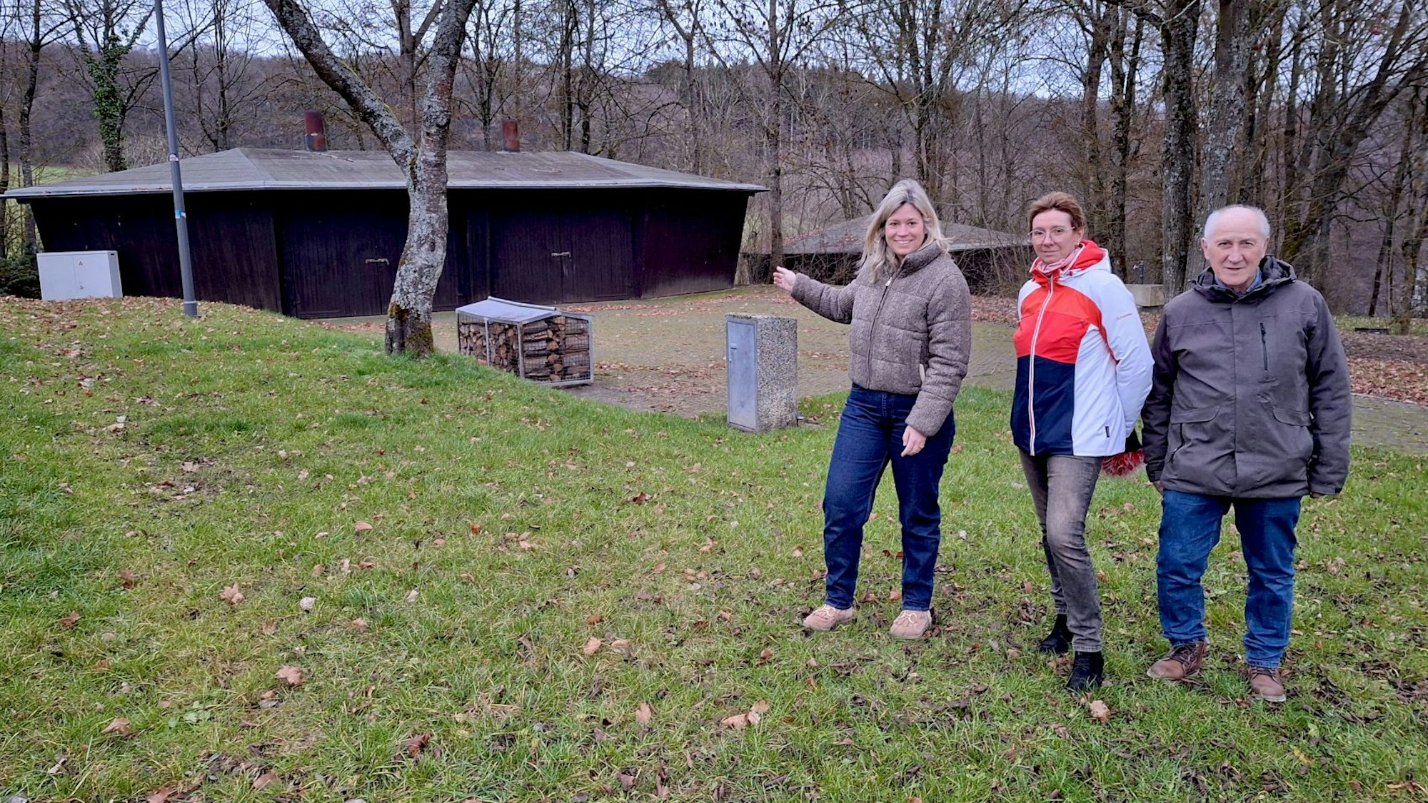 Zwei Frauen und ein Mann stehen auf einer Wiese am Freilinger See. Im Hintergrund ist eine Grillhütte.