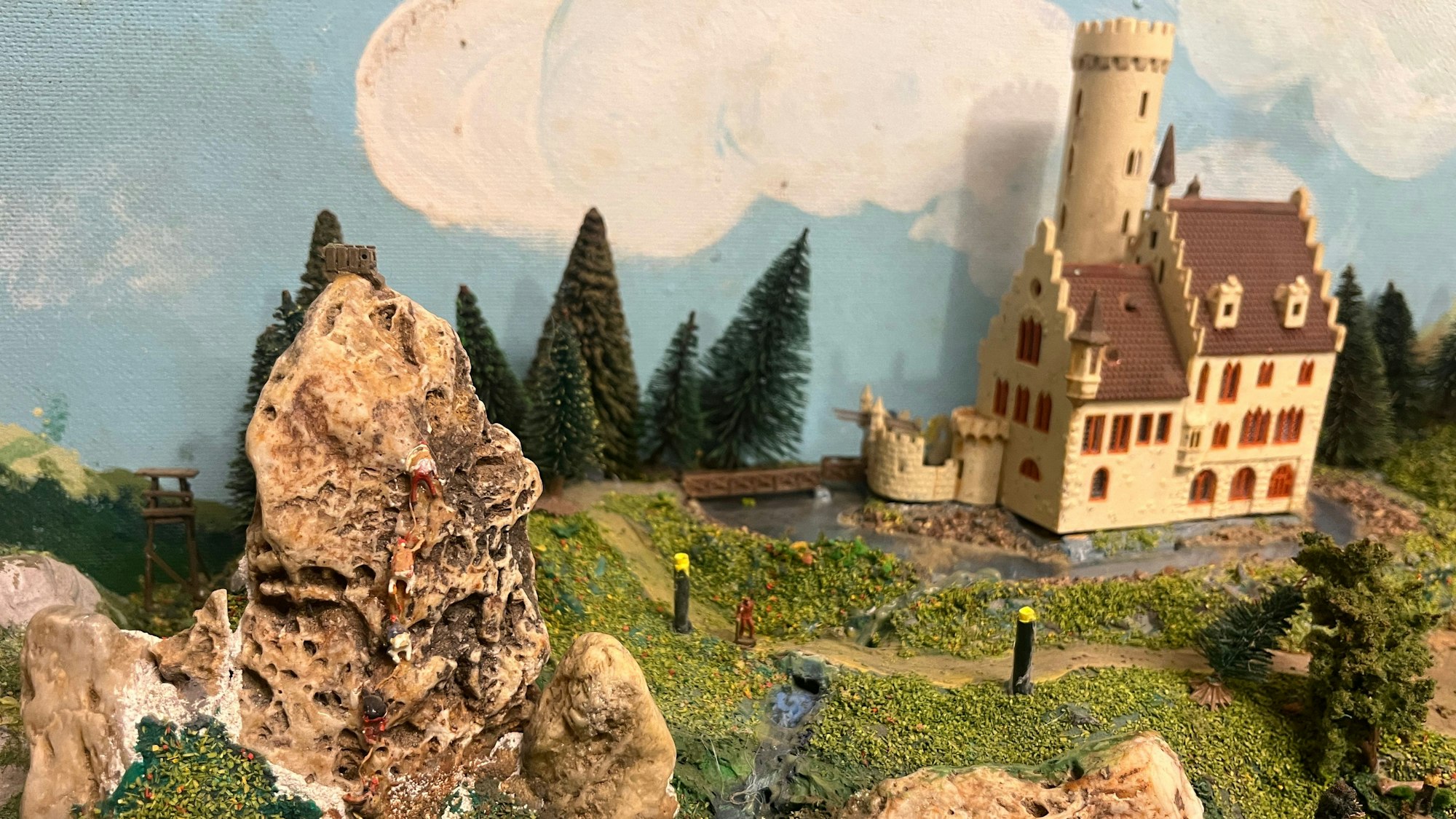In seiner Modelleisenbahn mit der Spur N gibt es ein Schloss, daneben klettern Alpinisten im Fels.