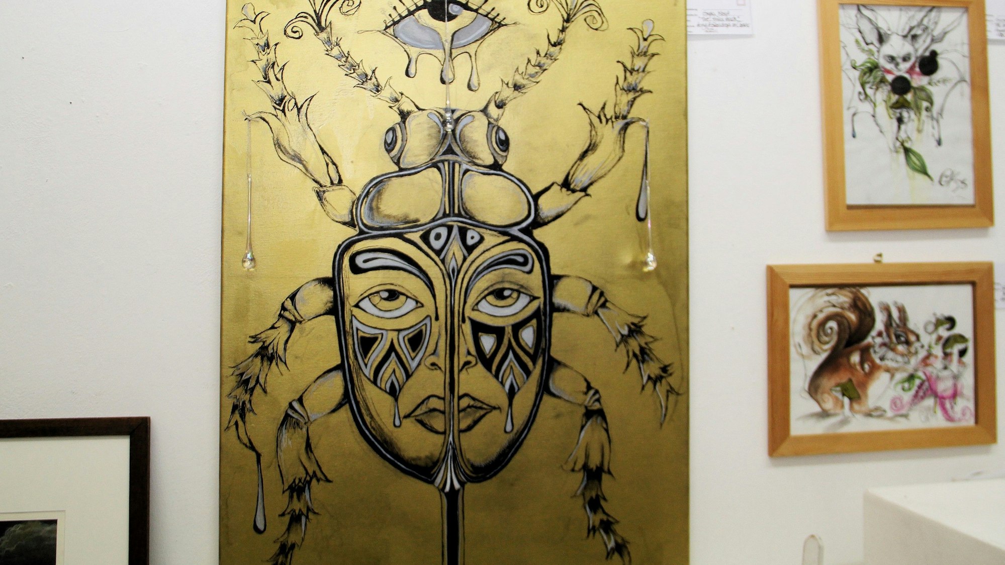 Ein großformatiges zeigt eine Maske, es ist in Goldtönen gehalten.