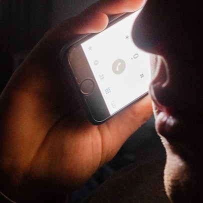 Das Symbolbild zeigt einen Gesichtsausschnitt im Halbdunkel, dazu eine Hand, die ein Telefon hält.
