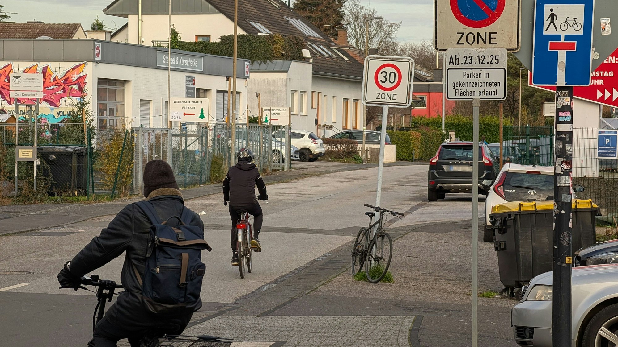 Das Foto zeigt zwei Radfahrer, die von der Kaulardstraße auf die Straße „Zum Komarhof“ abgebogen sind.