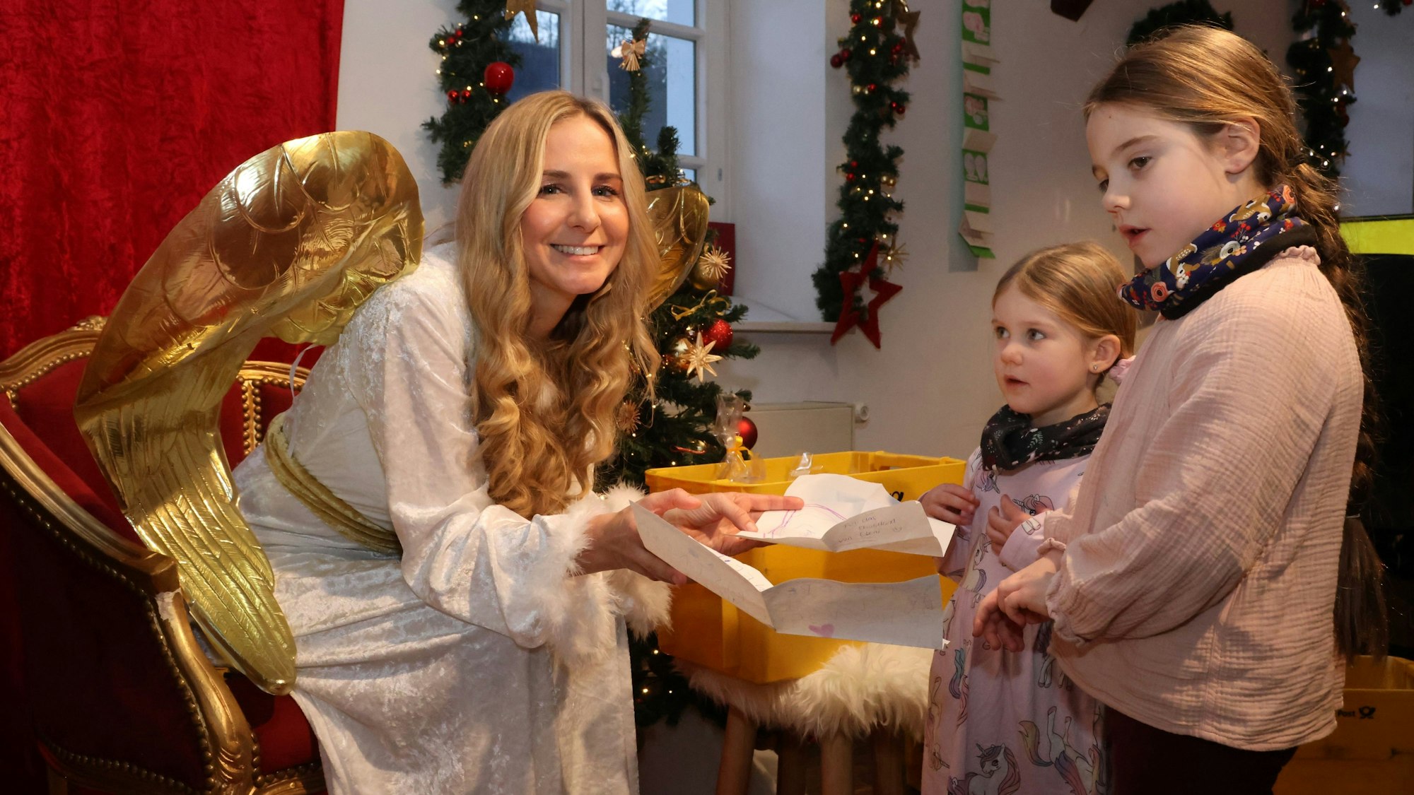 Das Christkind nimmt Wunschzettel von zwei Kindern entgegen.