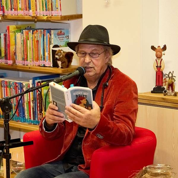 Günter Hochgürtel sitzt in einem roten Sessel im Literaturhaus in Nettersheim und liest aus einem Buch vor.