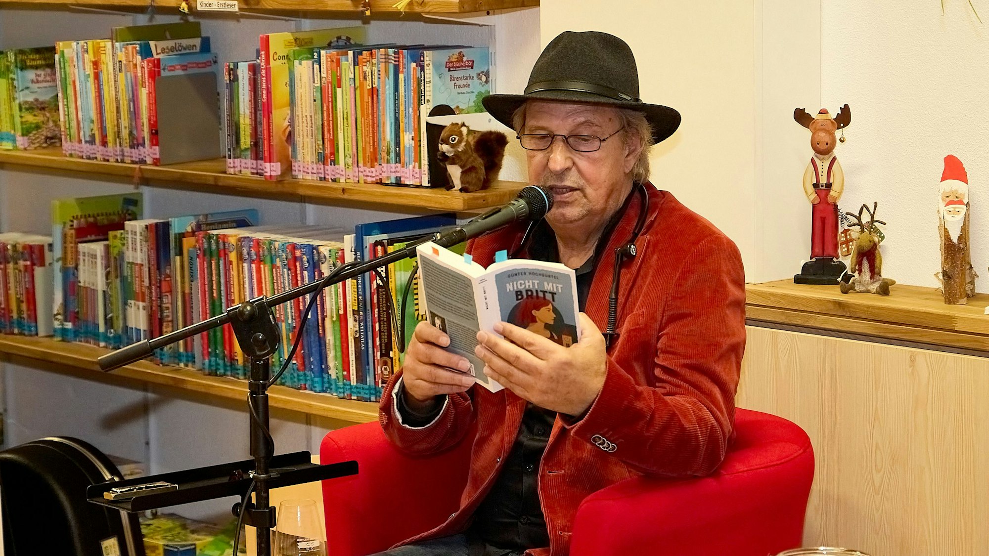 Günter Hochgürtel sitzt in einem roten Sessel im Literaturhaus in Nettersheim und liest aus einem Buch vor.