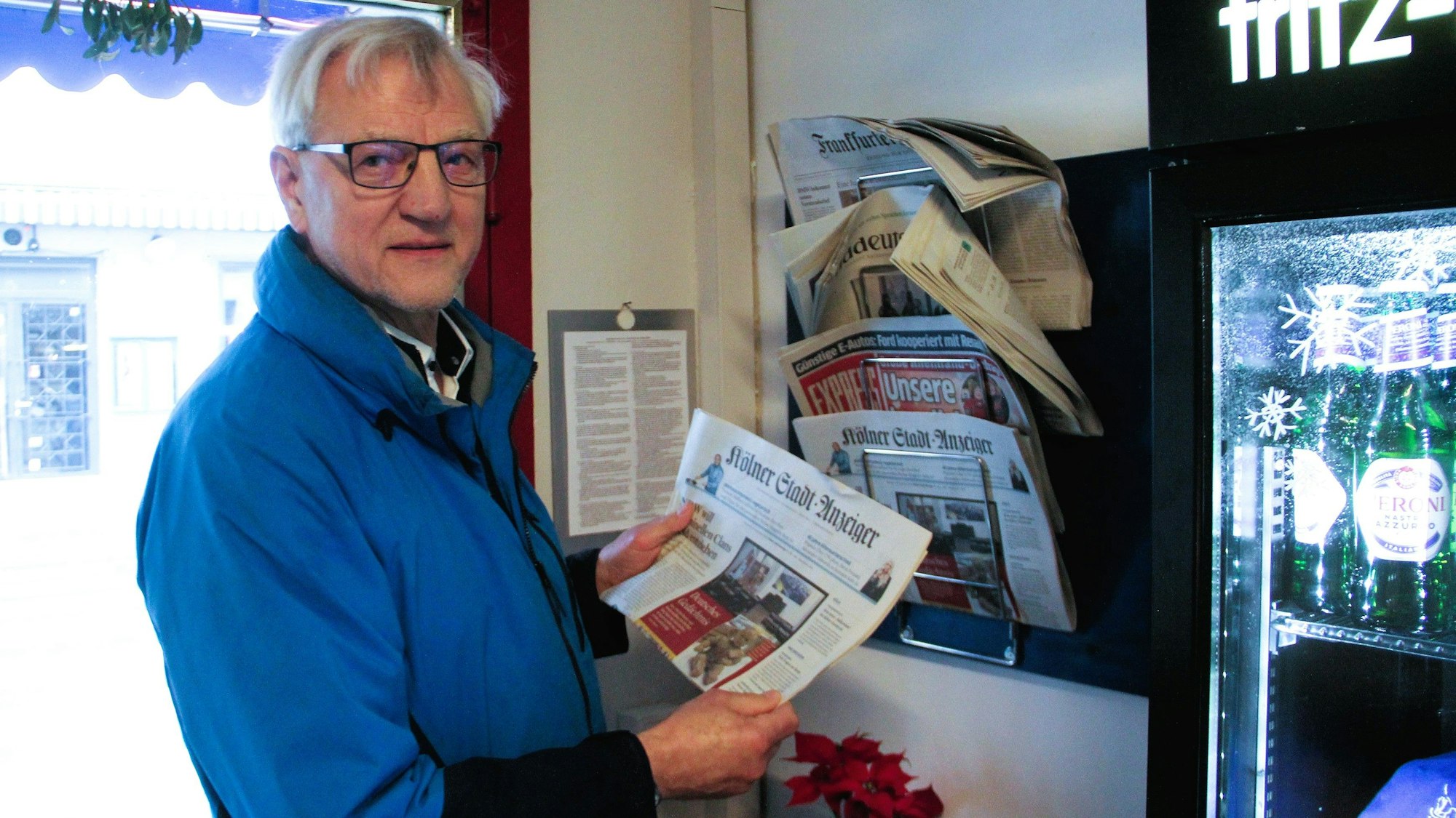 Ein Mann hält eine Ausgabe des „Kölner Stadt-Anzeiger“ in der Hand. Er steht in einem Büdchen.