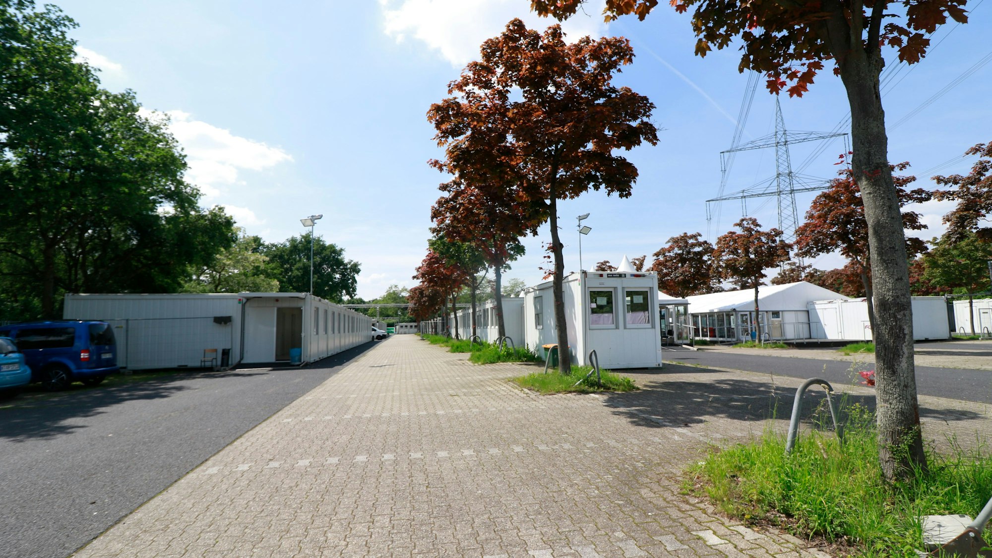 Auf einem Parkplatz stehen zahlreiche weiße Wohncontainer und ein großer Zeltbau.