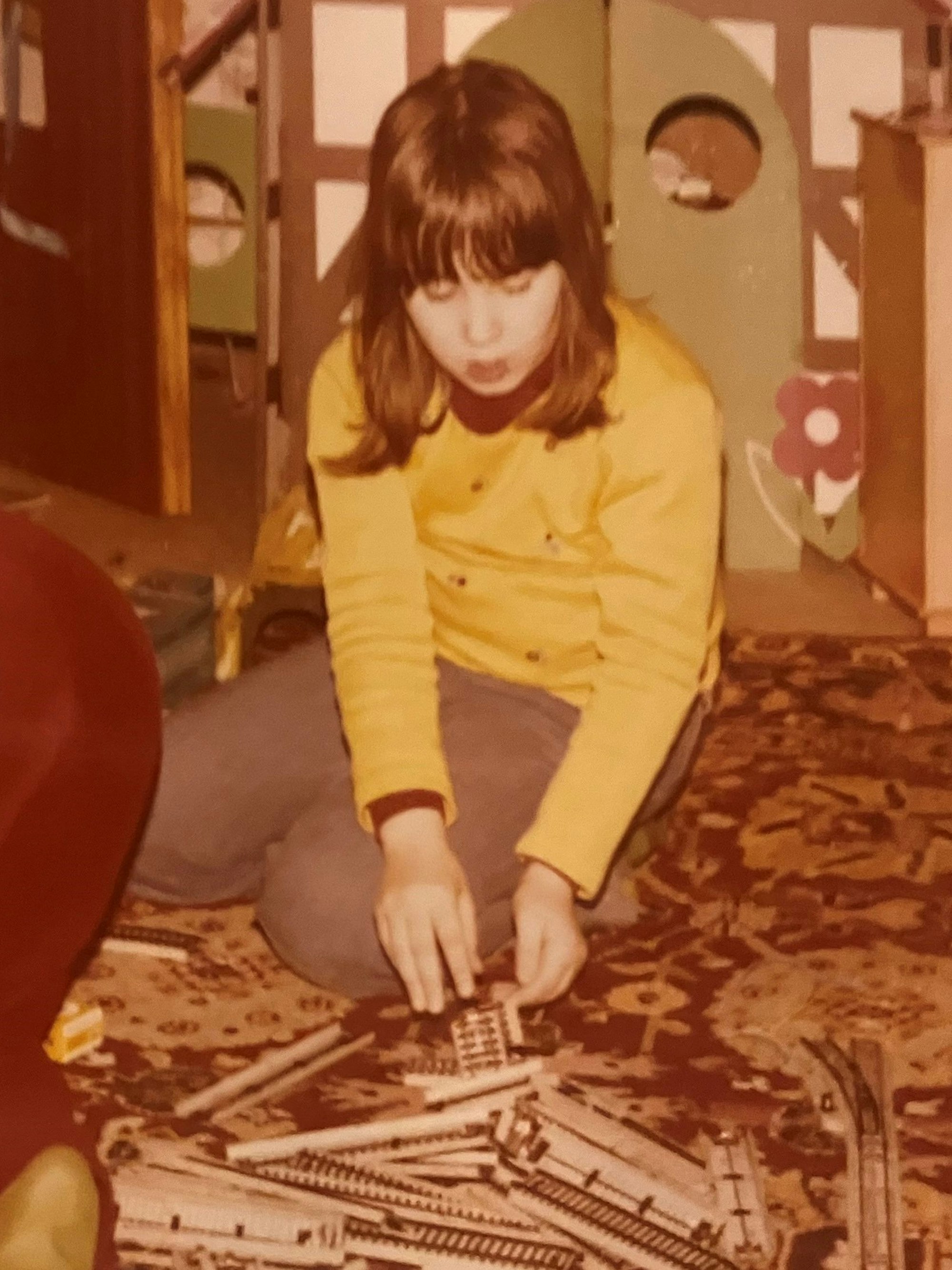 Ein Mädchen sitzt auf einem Teppichboden und schaut auf Schiene einer Modelleisenbahn.