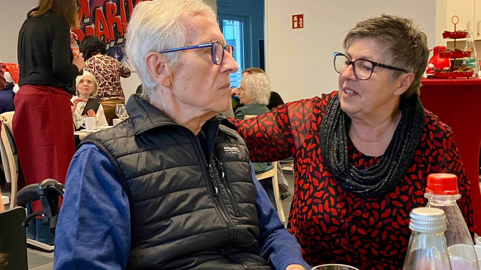 Das Bild zeigt die beiden Obengenannten an einem Tisch. Edith Rebmann legt einen Arm um ihren Mann.