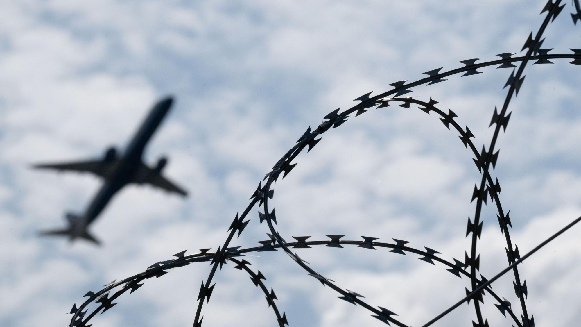 Ein Flugzeug mit Abschiebehäftlingen hebt am Flughafen hinter einem Zaun mit Natodraht ab.