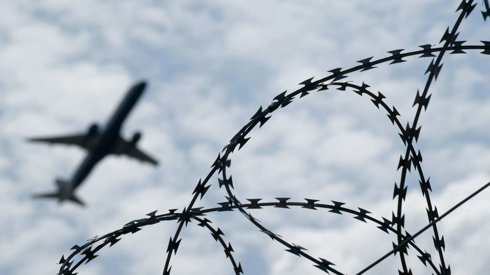Ein Flugzeug mit Abschiebehäftlingen hebt am Flughafen hinter einem Zaun mit Natodraht ab.