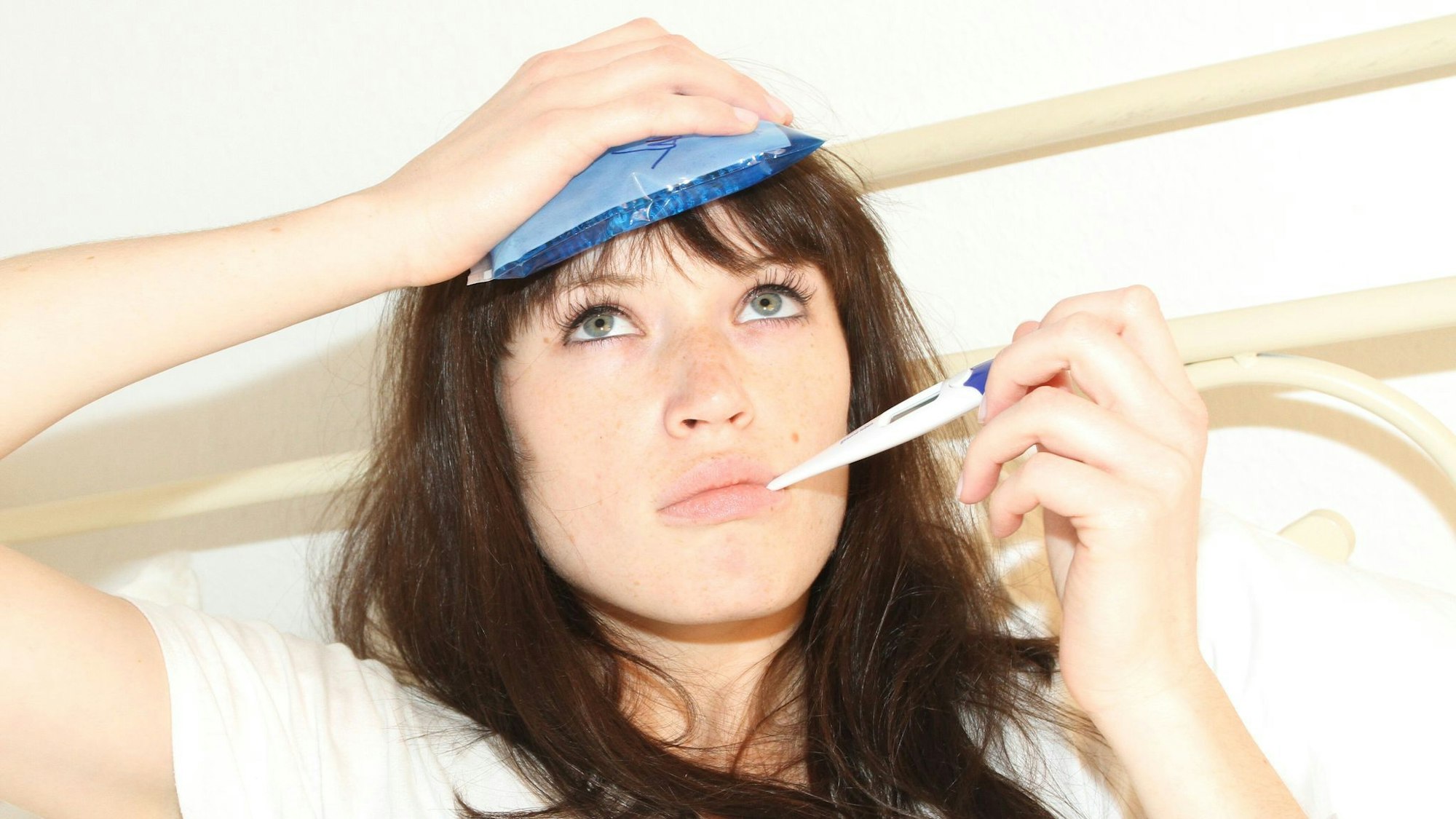 Eine Frau mit Fieberthermometer im Mund.