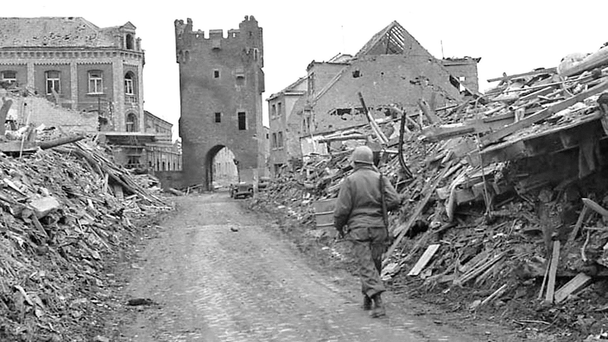 Ein Soldat geht zwischen Trümmerbergen auf das Stadttor zu.