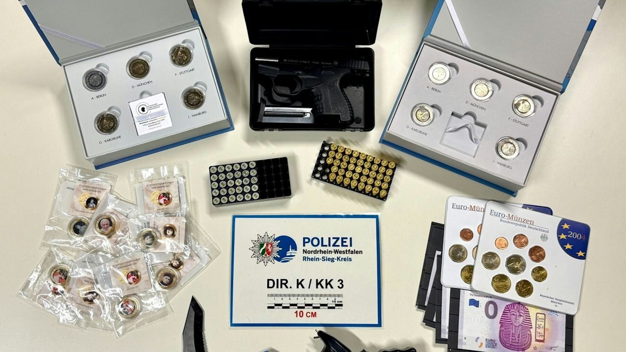 Sichergestellte Waffen und Beute liegen auf einem Tisch: eine Pistole, ein Messer, ein Elektroschocker und Münzen.