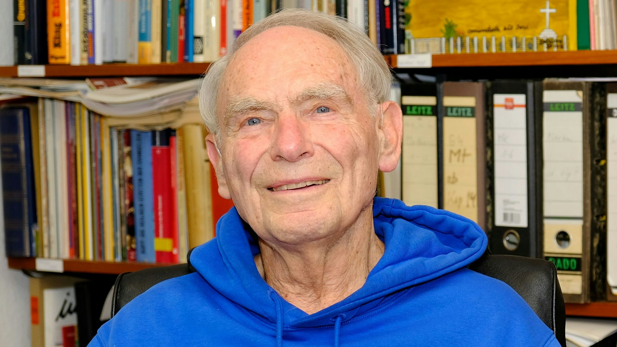 Dr. Herbert Kaefer (87), Pfarrer im Ruhestand aus Gemünd, sitzt in einem kobaltblauen Hoodie in seinem Arbeitszimmer.