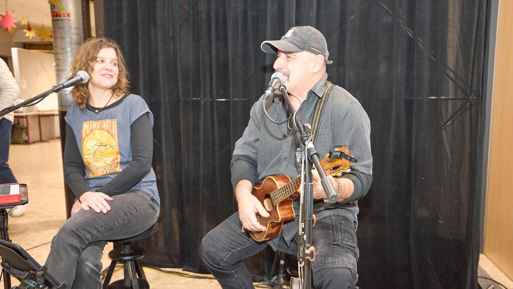 Das Foto zeigt zwei Musiker auf Stühlen sitzend am Mikrofon. Vassil Svechtarov spielt auf einer Gitarre und singt, Inga Beitz-Svechtarov schaut ihn an.