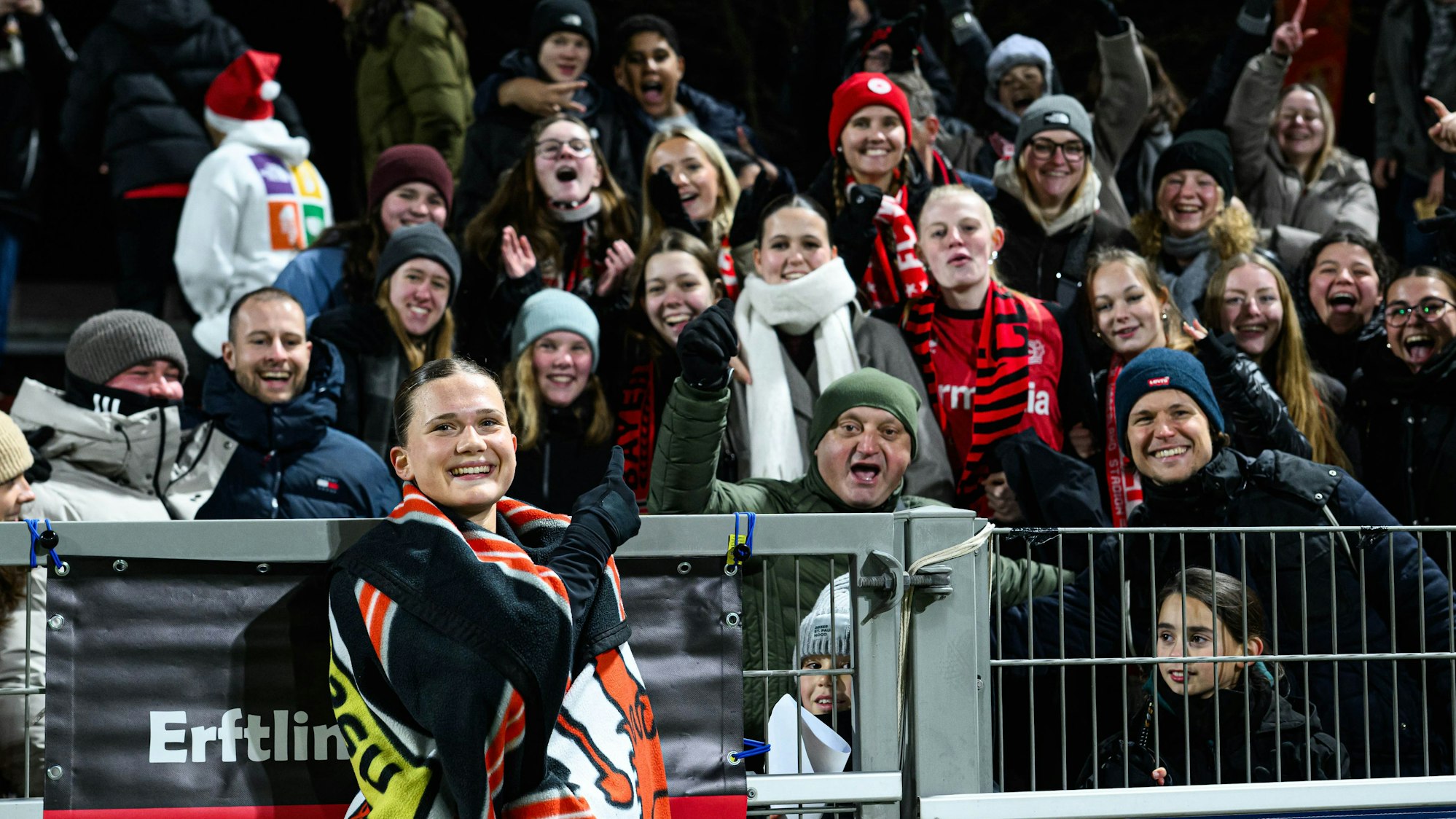 Julia Mickenhagen steht, in eine Decke gehüllt, vor dem Zaun hinter dem ihre Fans sind.