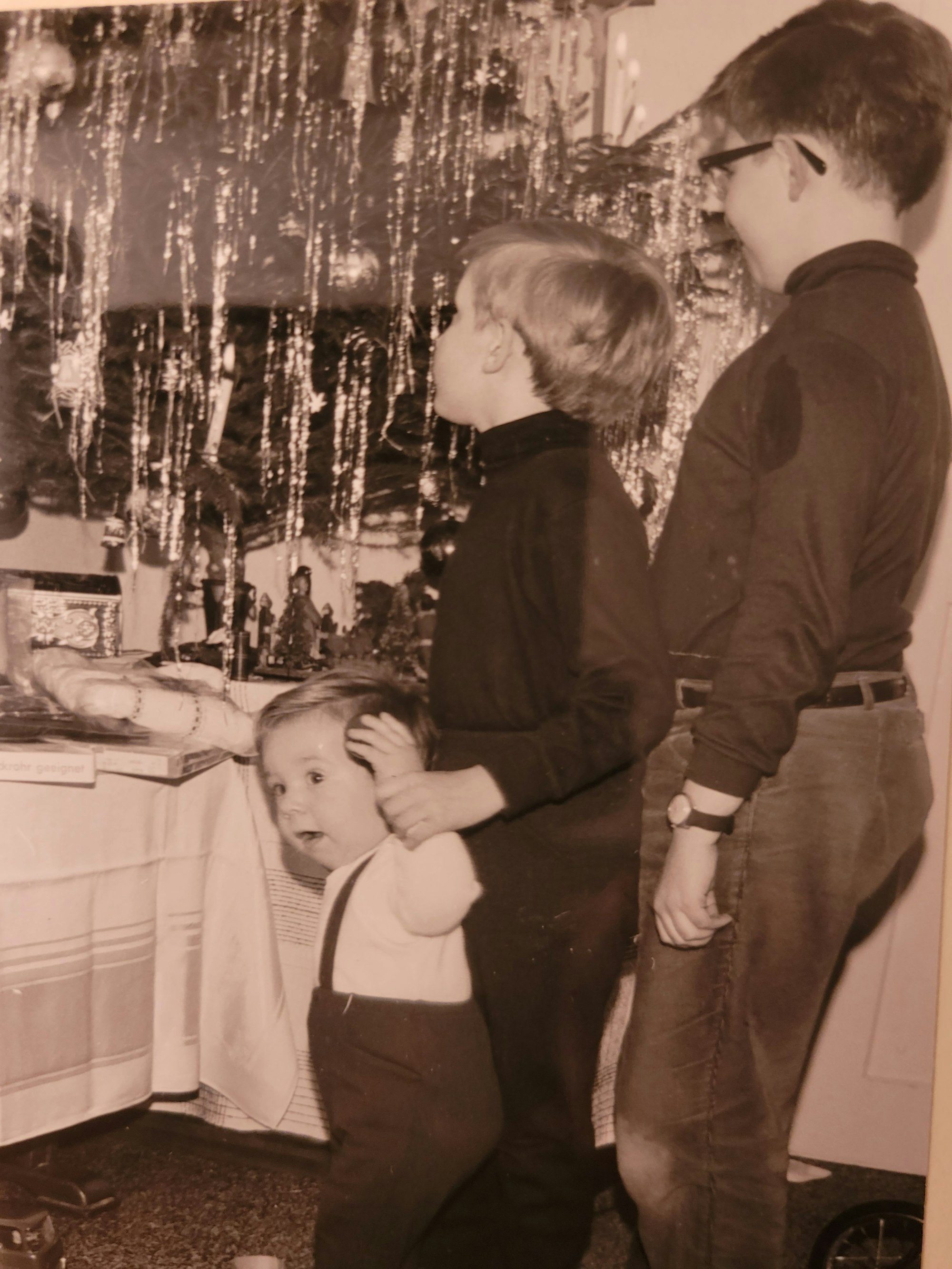 Drei Kinder stehen vor einem Weihnachtsbaum mit viel Lametta.