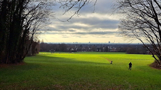 Über eine in der Sonne liegenden Wiese ist Bergisch Gladbach-Paffrath und am Horizont Köln zu sehen.