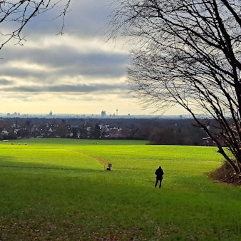 Über eine in der Sonne liegenden Wiese ist Bergisch Gladbach-Paffrath und am Horizont Köln zu sehen.