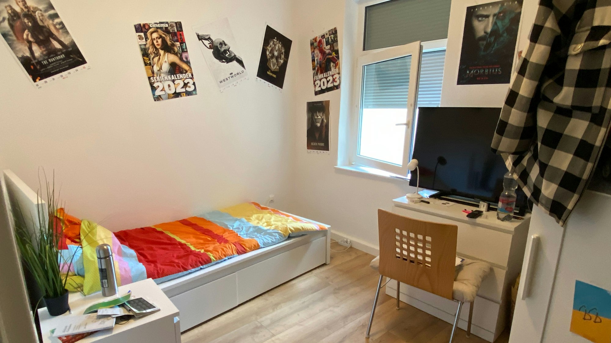 Ein Blick in eines der WG-Zimmer, der Boden ist aus hellem Holz, die Möbel sind weiß, an den Wänden hat der Bewohner Filmplakate gehängt.