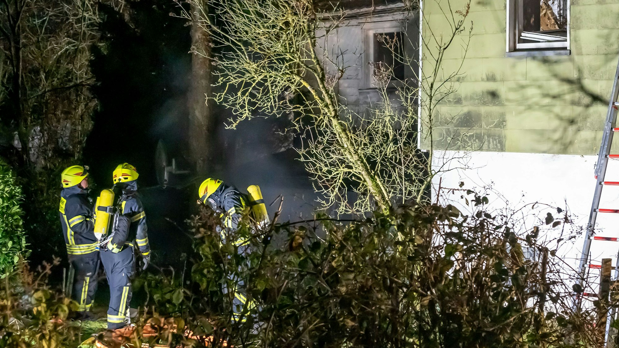 Drei Feuerwehrleute mit Atemschutz stehen vor einem Haus.