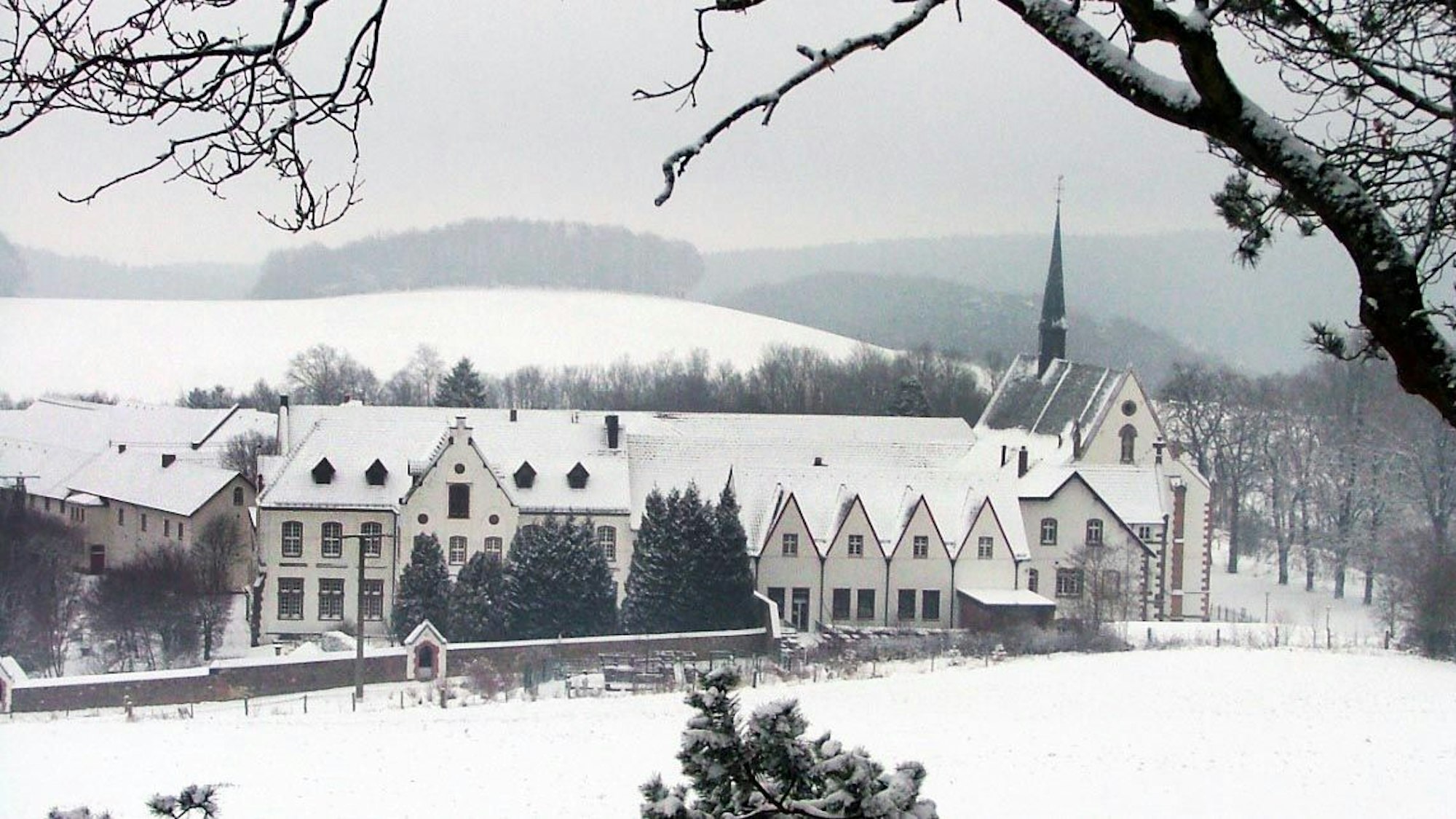 In der verschneiten Winterlandschaft sieht man die Gebäude von Kloster Mariawald.