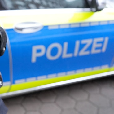 Ein Polizist mit Schusswaffe steht vor einem Einsatzfahrzeug der Polizei.
