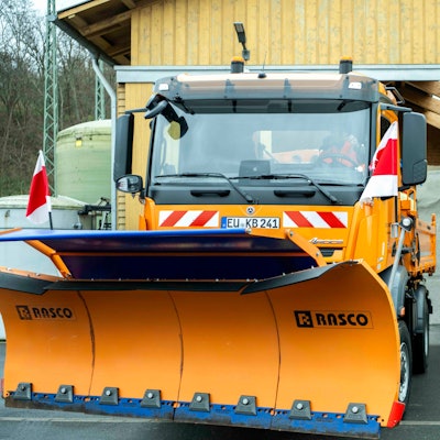 Ein orangefarbenes Schneeräumfahrzeug steht abfahrbereit vor der Halle, in der ein Berg Streusalz zu sehen ist.