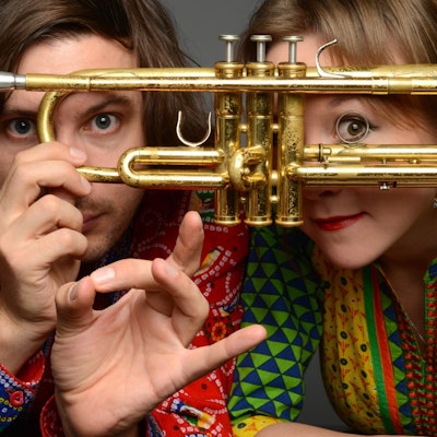 Die Kölner Jazz-Musiker Tamara Lukasheva und Matthias Schriefl schauen durch eine Trompete.