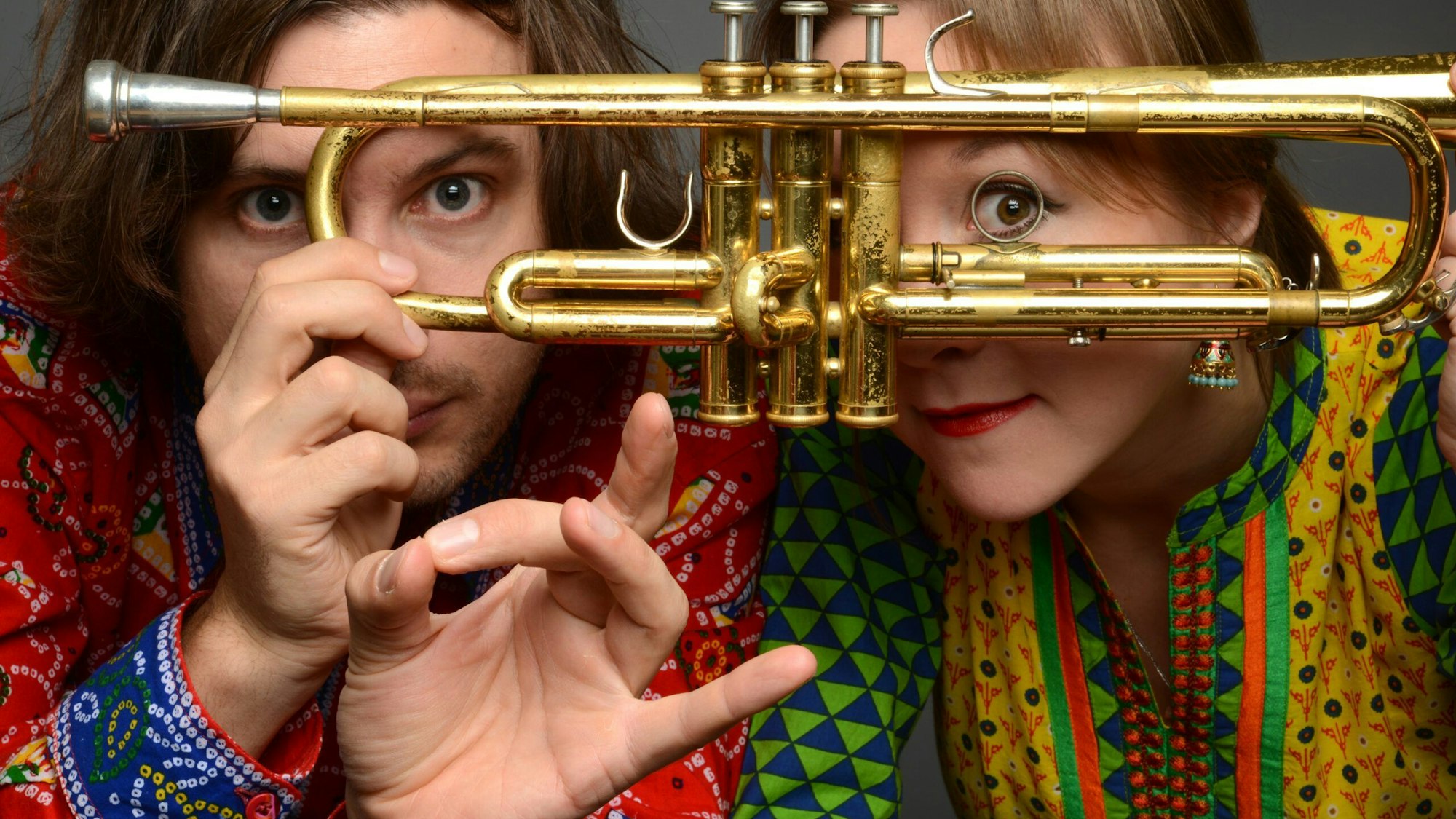 Die Kölner Jazz-Musiker Tamara Lukasheva und Matthias Schriefl schauen durch eine Trompete.