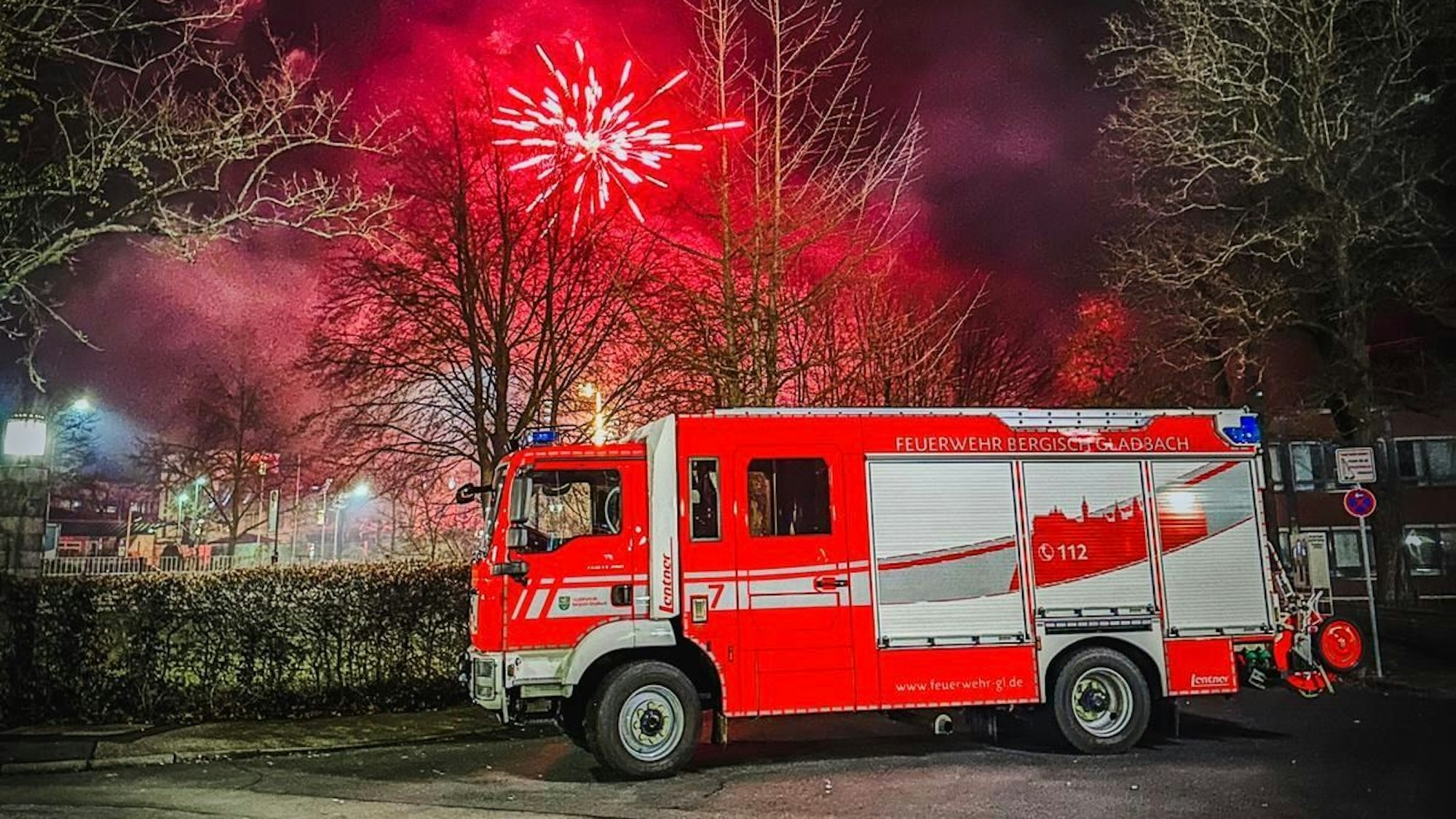 Ein Feuerwehrwagen ist vor einem mit Feuerwerk bedeckten Himmel zu sehen.
