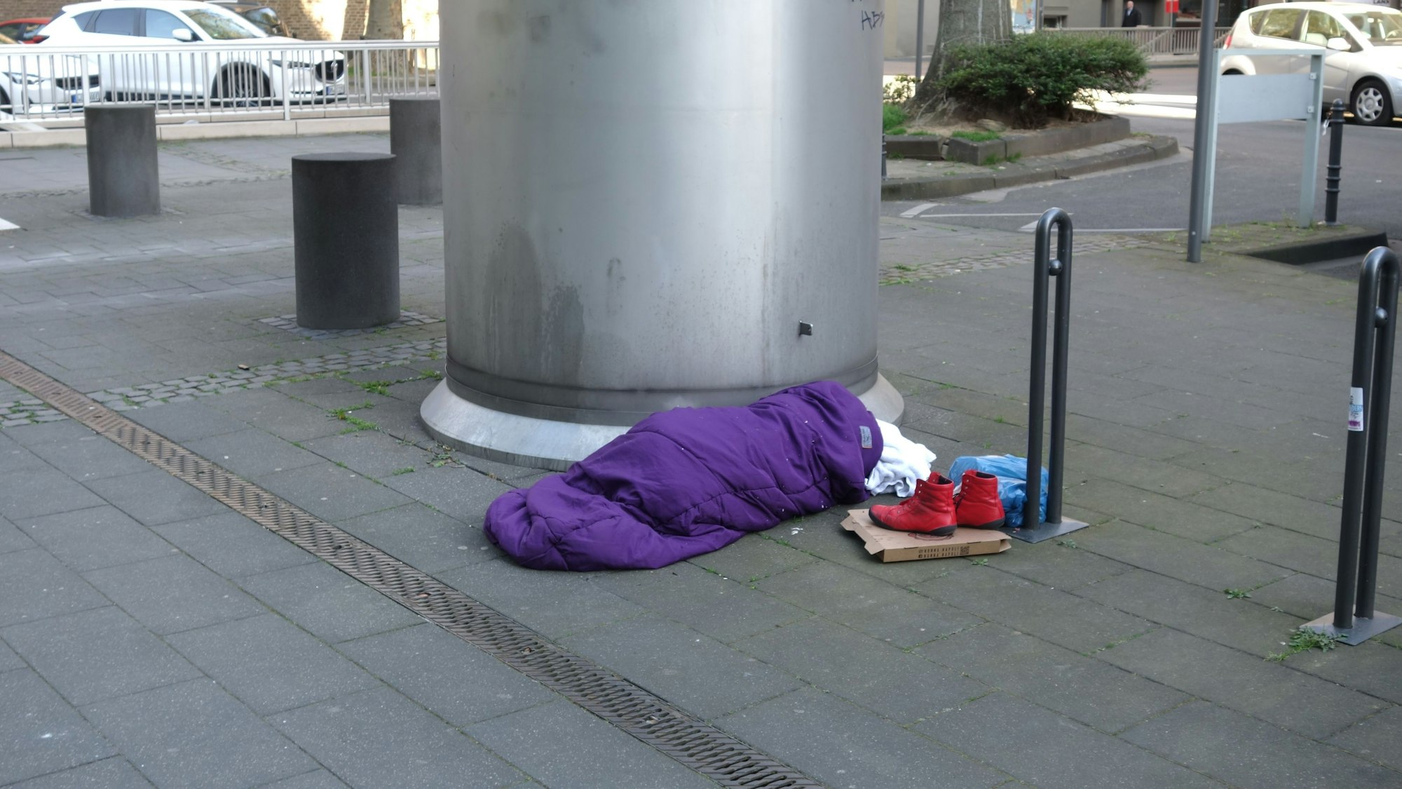 Eine obdachlose Frau schläft, eingewickelt in einem Schlafsack, am Appellhofplatz auf der Straße.