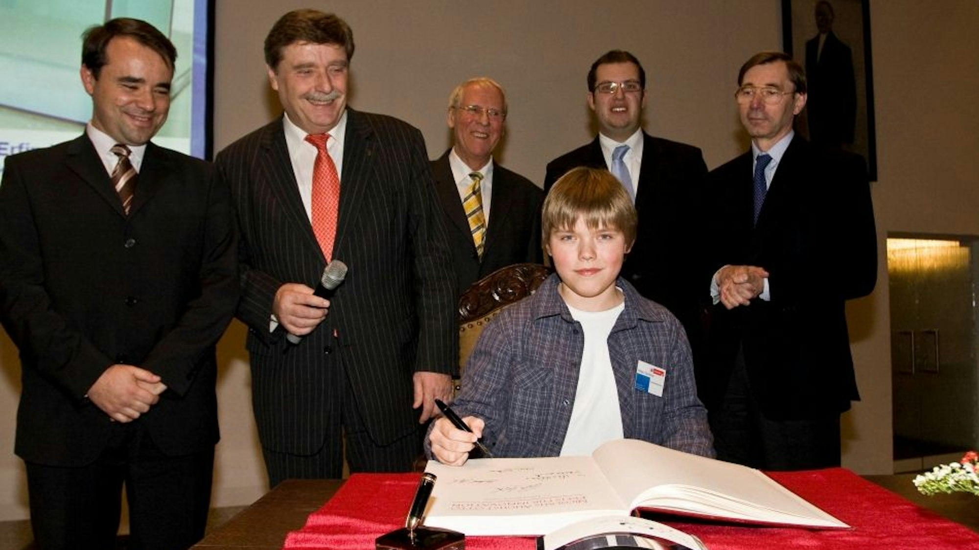Im Beisein des damaligen Kölner Oberbürgermeisters Fritz Schramma (2.v.l.) trug sich Kilian Günthner ins Goldene Buch der Stadt ein. Er sitzt an einem Tisch mit dem Füller in der Hand.
