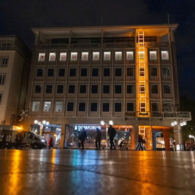 26.10.2025, Köln: Die Himmelsleiter ist eine Kunstinstallation an der Fassade des Domforums. Bei der etwa 20 Meter langen Leiter handelt es sich um ein Kunstwerk aus gold-gelb lackiertem Aluminium und Neonglas. Es leuchtet bis ins nächste Jahr hinein, stets ab der Dämmerung. Foto: Uwe Weiser