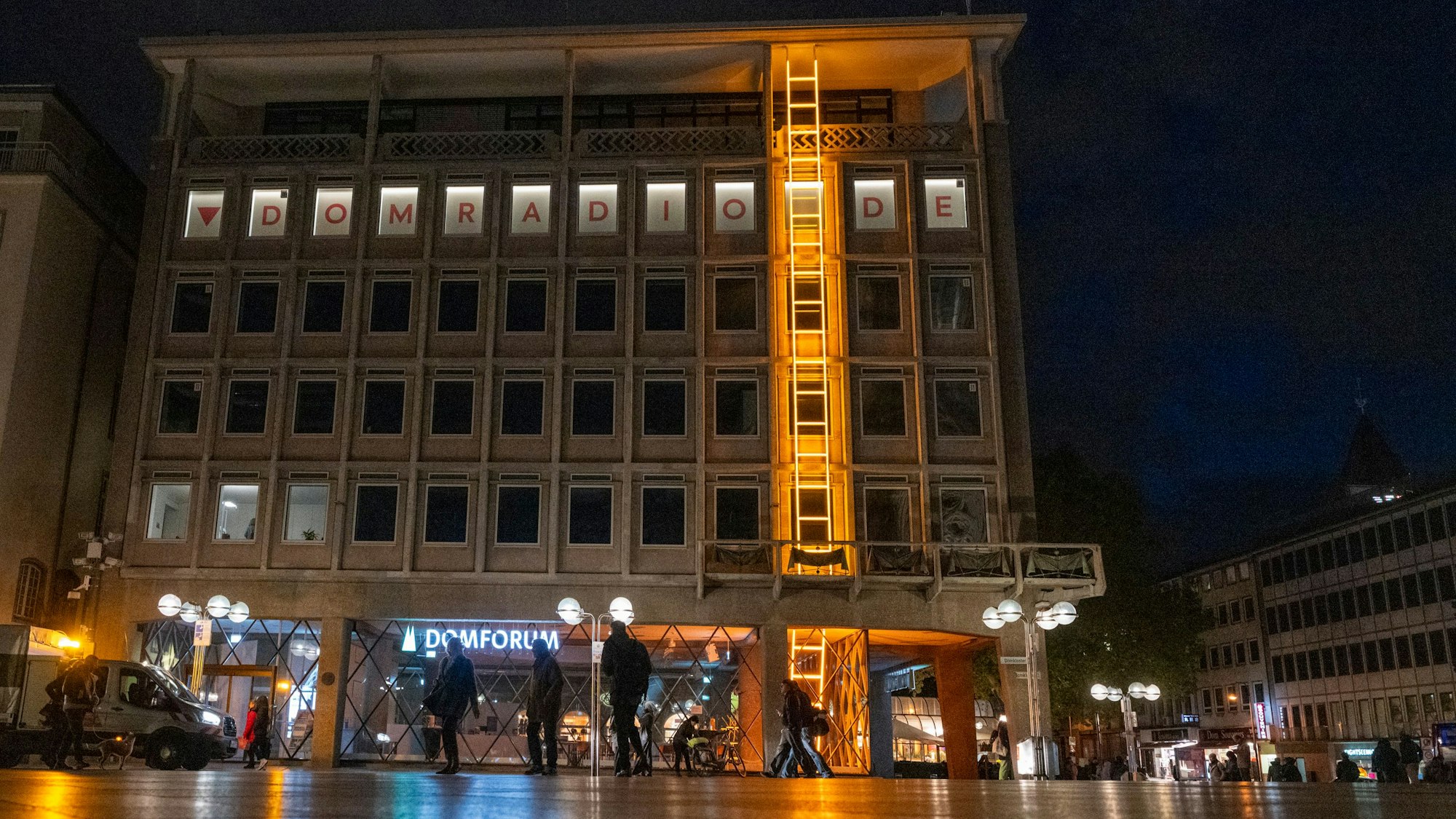 26.10.2025, Köln: Die Himmelsleiter ist eine Kunstinstallation an der Fassade des Domforums. Bei der etwa 20 Meter langen Leiter handelt es sich um ein Kunstwerk aus gold-gelb lackiertem Aluminium und Neonglas. Es leuchtet bis ins nächste Jahr hinein, stets ab der Dämmerung. Foto: Uwe Weiser